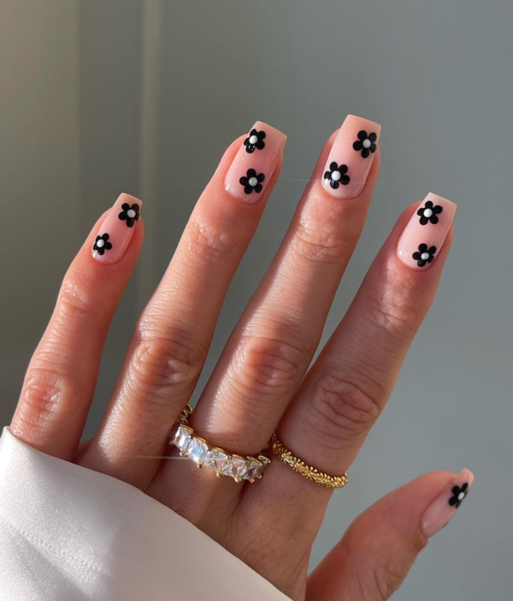 Black floral nails with elegant coffin shaped black and white flowers - bold hand showcasing black base with elegant black and white flower petals, featuring green leaves and stems on coffin-shaped nails